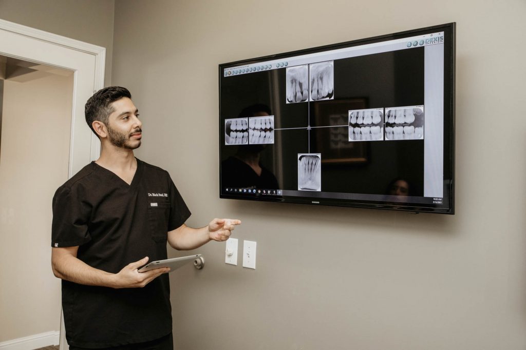 a dentist pointing at a tv screen displaying x-rays of teeth