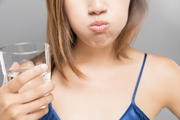 woman holding a glass of water with water in her mouth